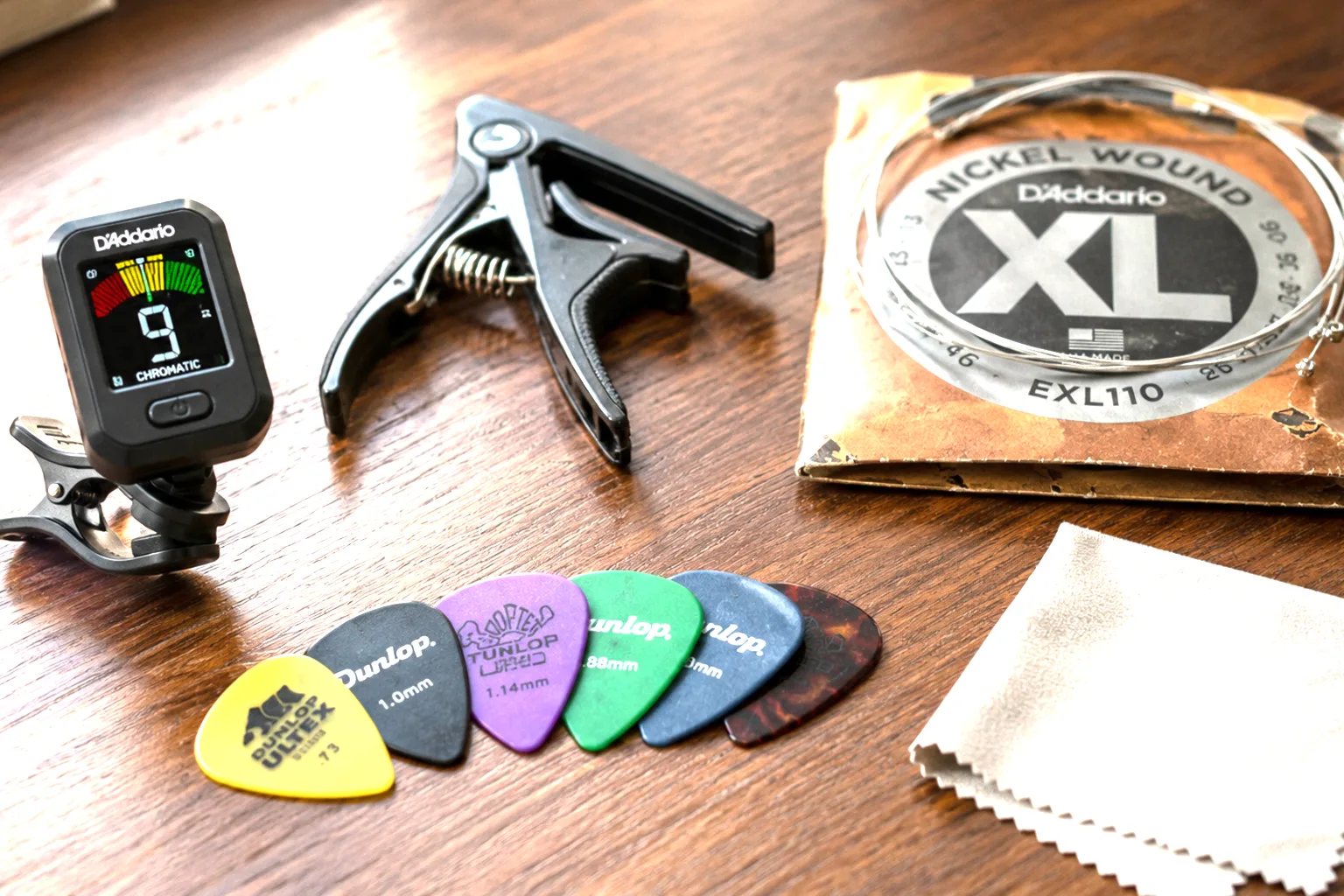 Guitar accessories including picks, a capo, tuner, and strings on a desk