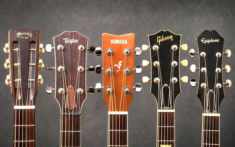 Row of acoustic guitar headstocks from different manufacturers showing Martin, Taylor, Yamaha, Gibson, and Epiphone logos