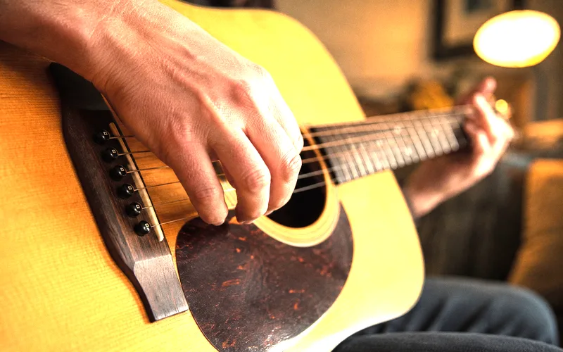 Guitarist fingerpicking an acoustic guitar showing right hand technique over the soundhole