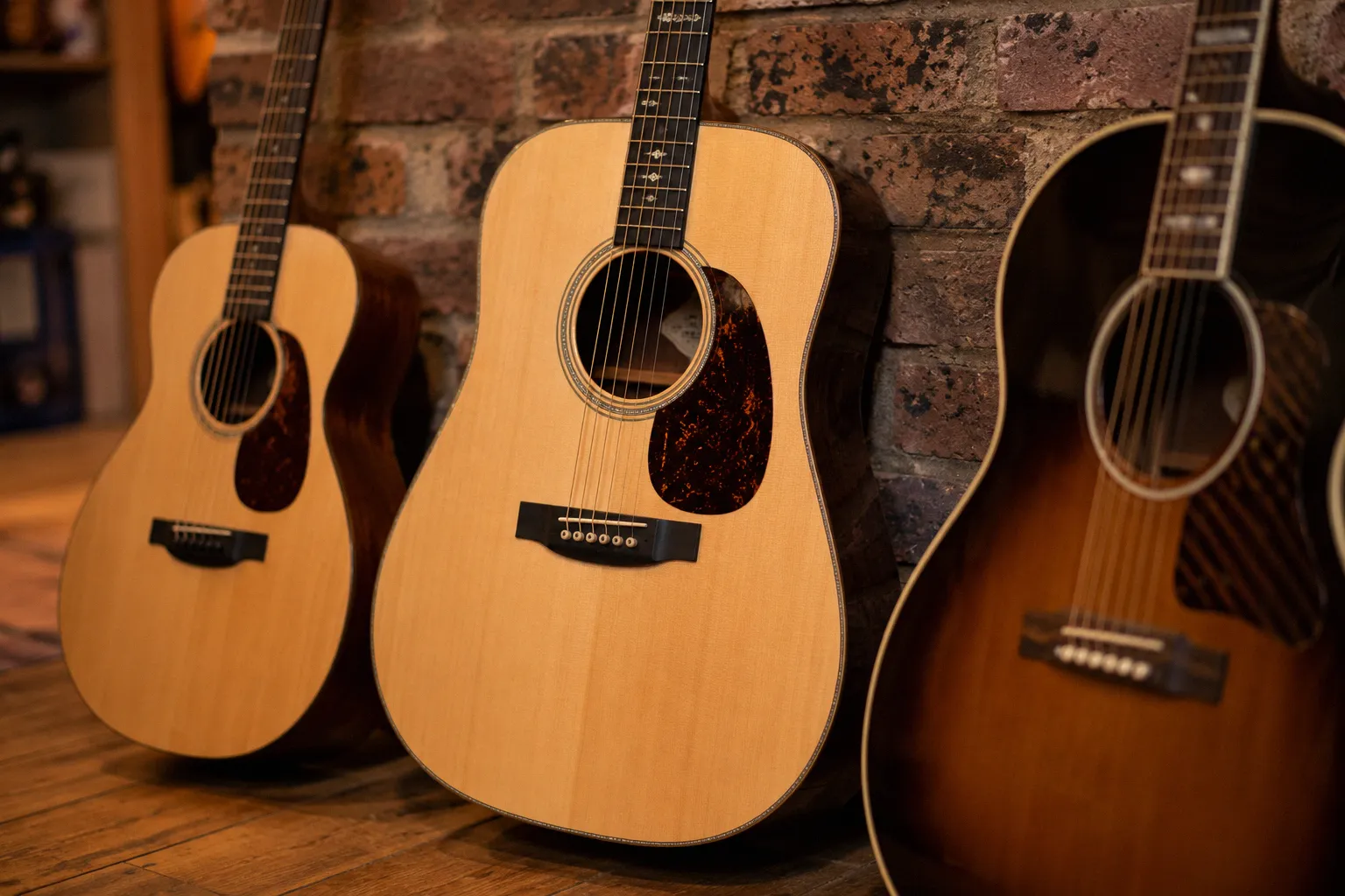 Three acoustic guitars leaning against a brick wall in a guitar shop