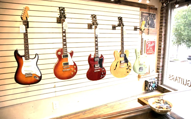 Row of different electric guitar types in a guitar shop including Stratocaster, Les Paul, SG, semi-hollow, and offset models available for testing