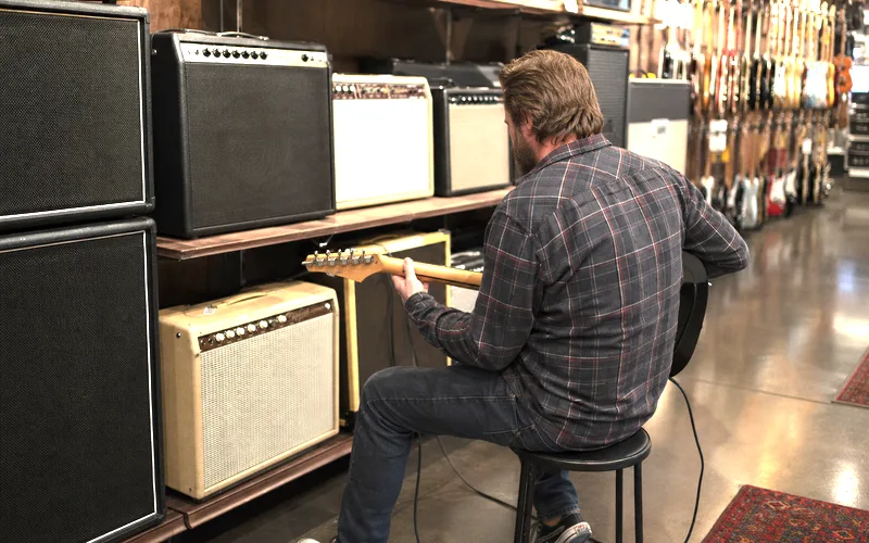 Guitarist comparing different amplifier types in a music store