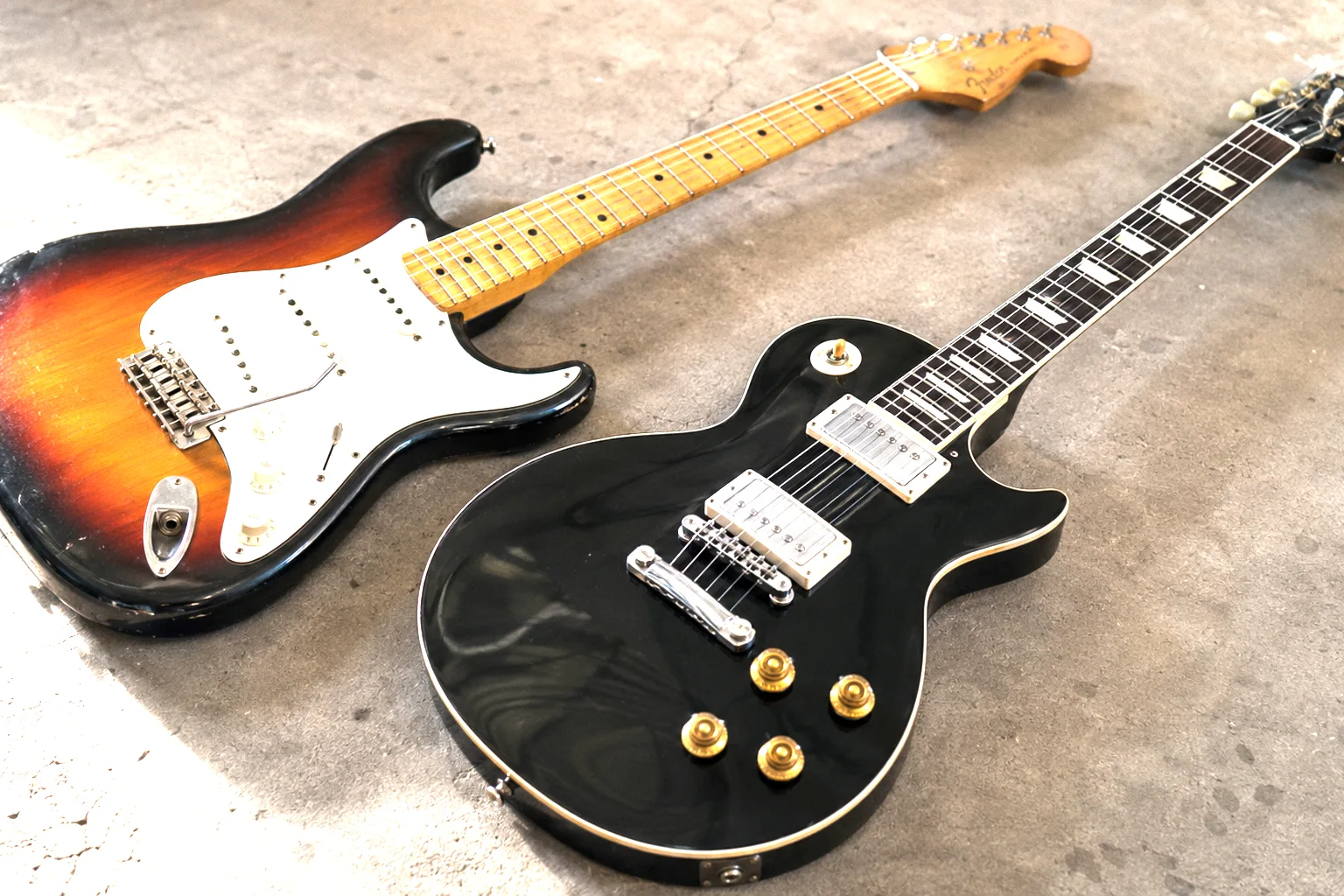 Sunburst Stratocaster and black Les Paul lying on a concrete surface