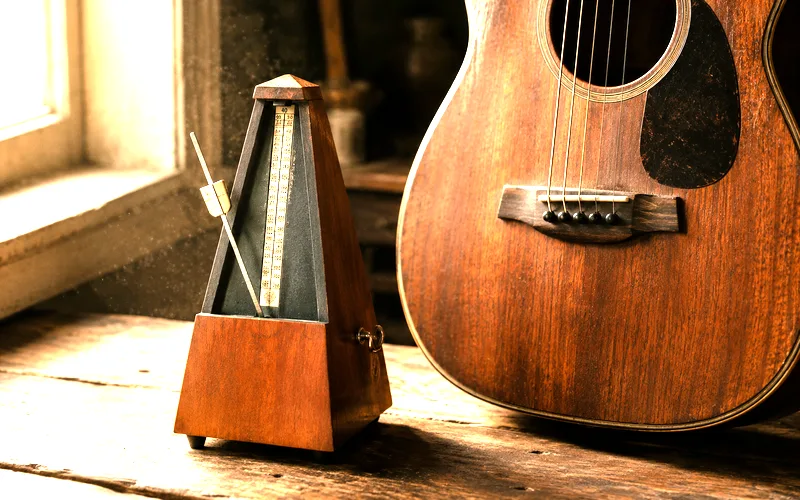 Mechanical metronome ticking next to an acoustic guitar on a wooden surface