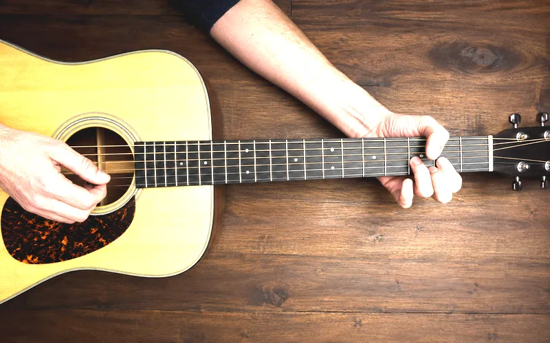 Overhead view of hands forming an open G chord on an acoustic guitar