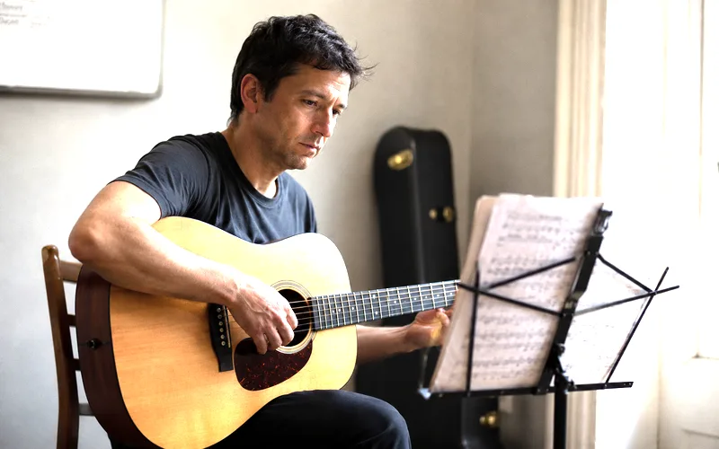 Frustrated guitarist sitting with an acoustic guitar looking thoughtfully at sheet music