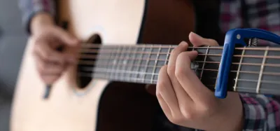 Capo clamped on a guitar neck while tuning the strings with a clip-on tuner