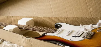 Acoustic guitar packed in a hardshell case inside a shipping box with padding