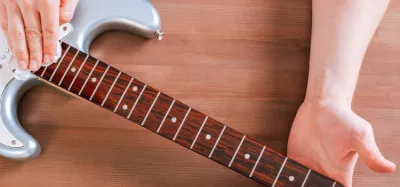 Close-up of a guitar neck and fretboard being wiped clean with a soft cloth