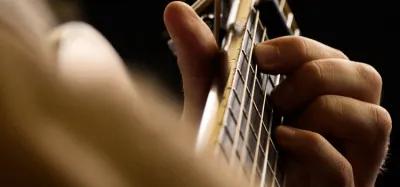 Close-up of a guitarist's hand fretting chords, showing the forearm and finger muscles used while playing