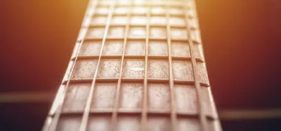 Close-up of a hand fretting a chord on a curved guitar fingerboard