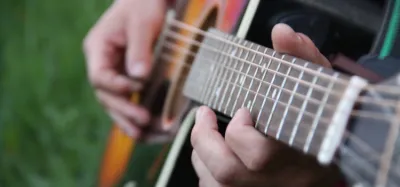 Close-up of a flatpick striking acoustic guitar strings during a beginner flatpicking song
