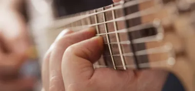 Close-up of a guitarist's fingers pressing steel strings on a fretboard