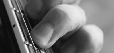 Close-up of a guitarist's fingertips pressing steel strings to build calluses