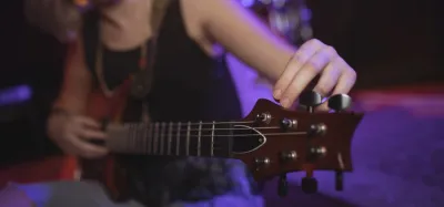 Close-up of a guitar headstock and tuning pegs while adjusting string tension