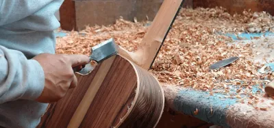 Luthier shaping the body of a guitar on a workbench with hand tools