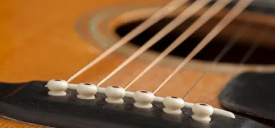 Hands restringing an acoustic guitar at the headstock and tuning pegs