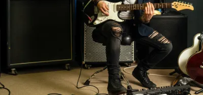 Guitarist setting up a looper pedal on a pedalboard connected to an amp