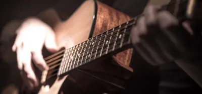Hands playing a fingerstyle pattern on an acoustic guitar