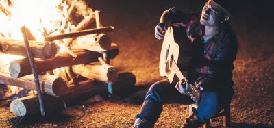 Musician playing a lightweight acoustic guitar beside a campfire