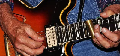 Guitarist playing slide guitar with a metal slide on the fretboard