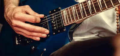 Thick guitar pick held against the strings of an electric guitar for metal playing