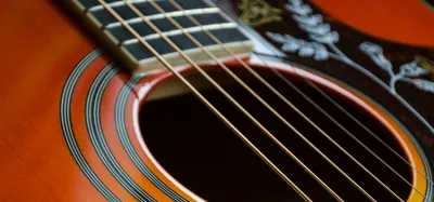 Acoustic guitar neck and strings showing the high action and thick strings that make it harder to play
